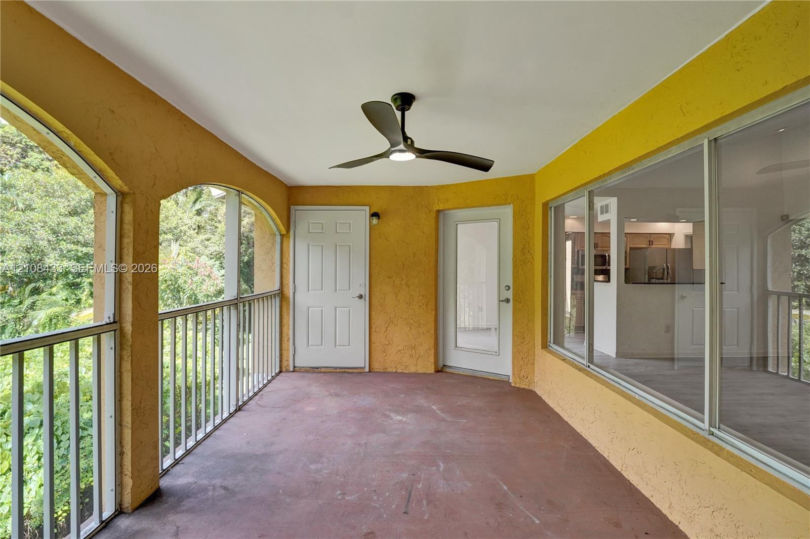 Covered balcony featuring arched architectural openings, metal railing, concrete flooring, and a ceiling fan with integrated lighting