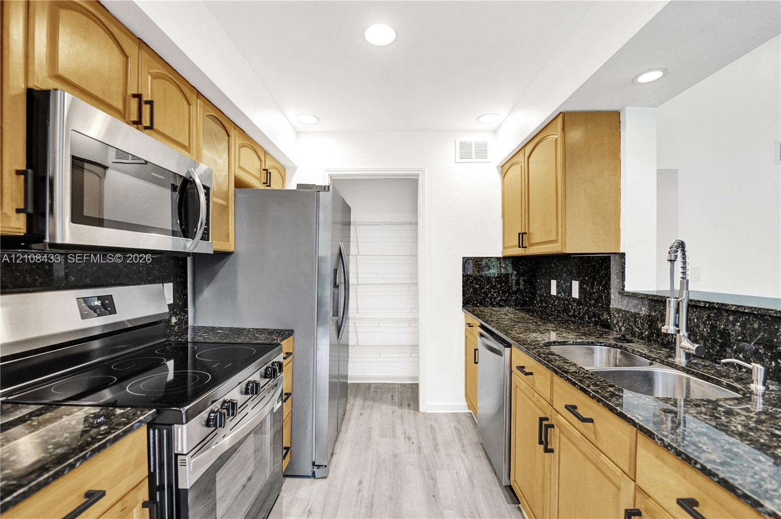 Kitchen featuring natural finish cabinetry, dark stone countertops, stainless steel appliances, a pull-down kitchen faucet, and wood-finish flooring Kitchen featuring natural finish cabinetry, dark stone countertops, stainless steel appliances, a pull-down kitchen faucet, and wood-finish flooring