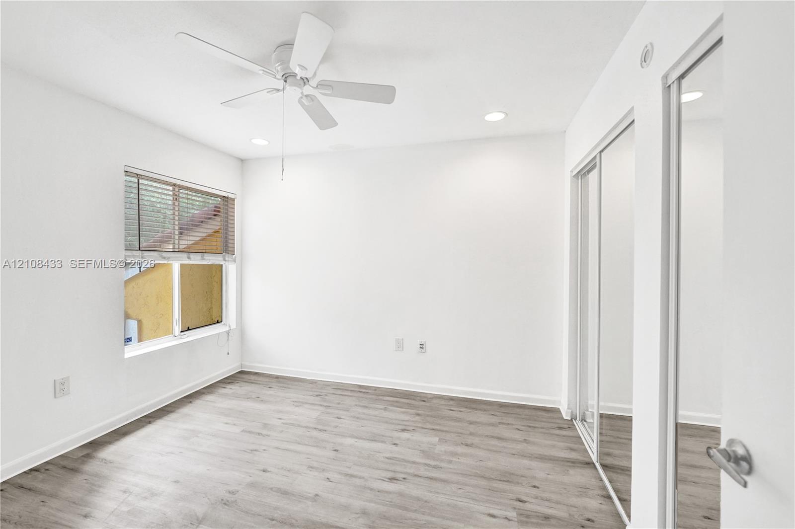 Neutral-toned wood-finish flooring, ceiling fan, recessed lighting, and mirrored sliding closet doors