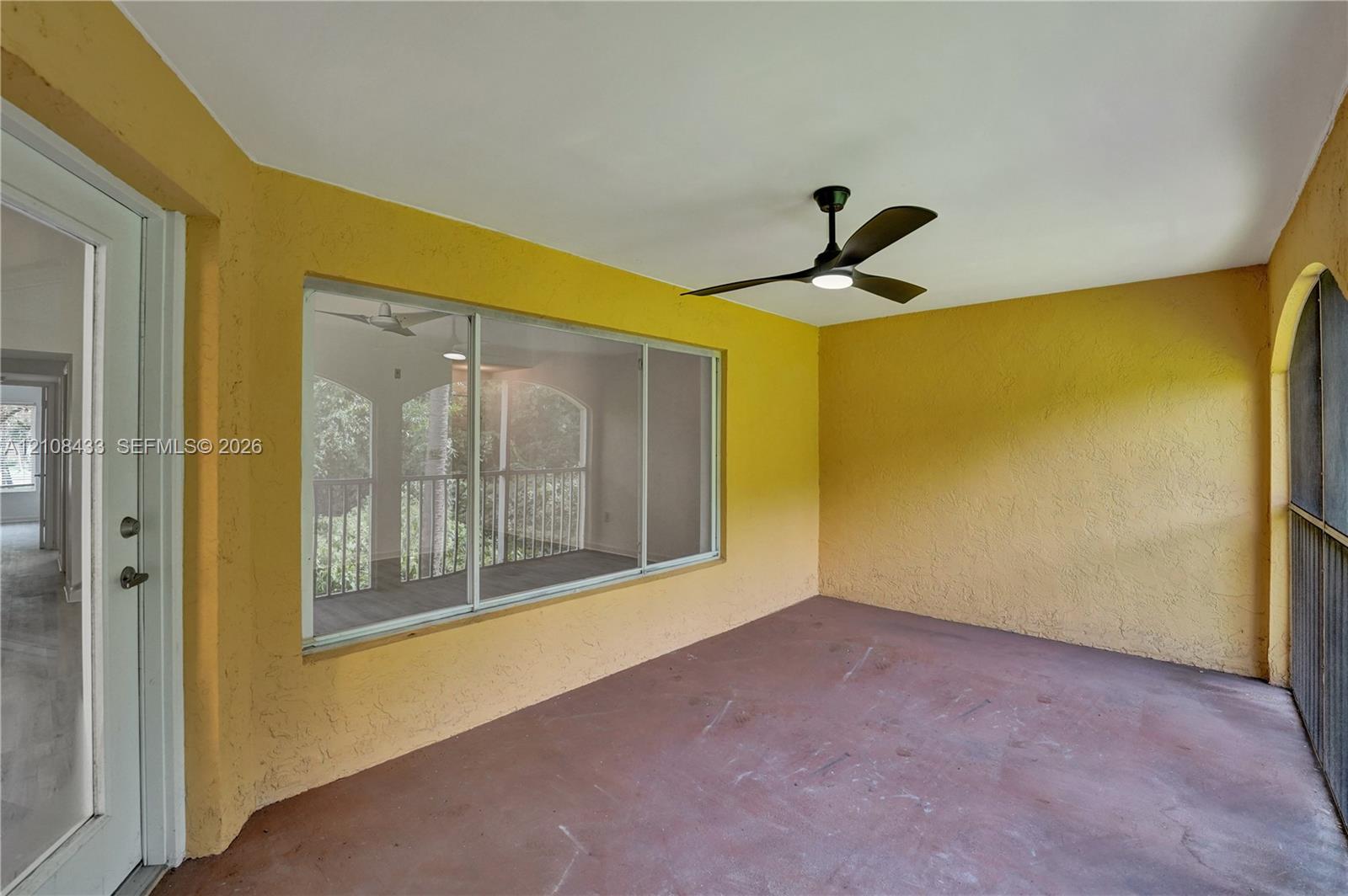 Covered porch featuring textured walls, concrete flooring, a ceiling fan with integrated lighting, and large sliding windows