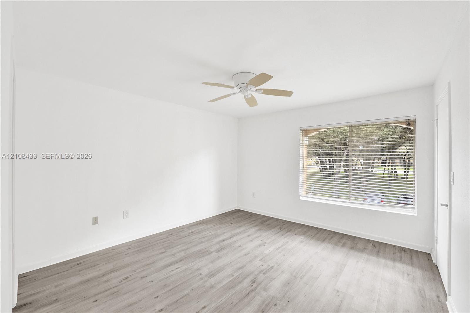 Neutral-toned walls, wood-finish flooring, ceiling-mounted fan, and a large window with horizontal blinds
