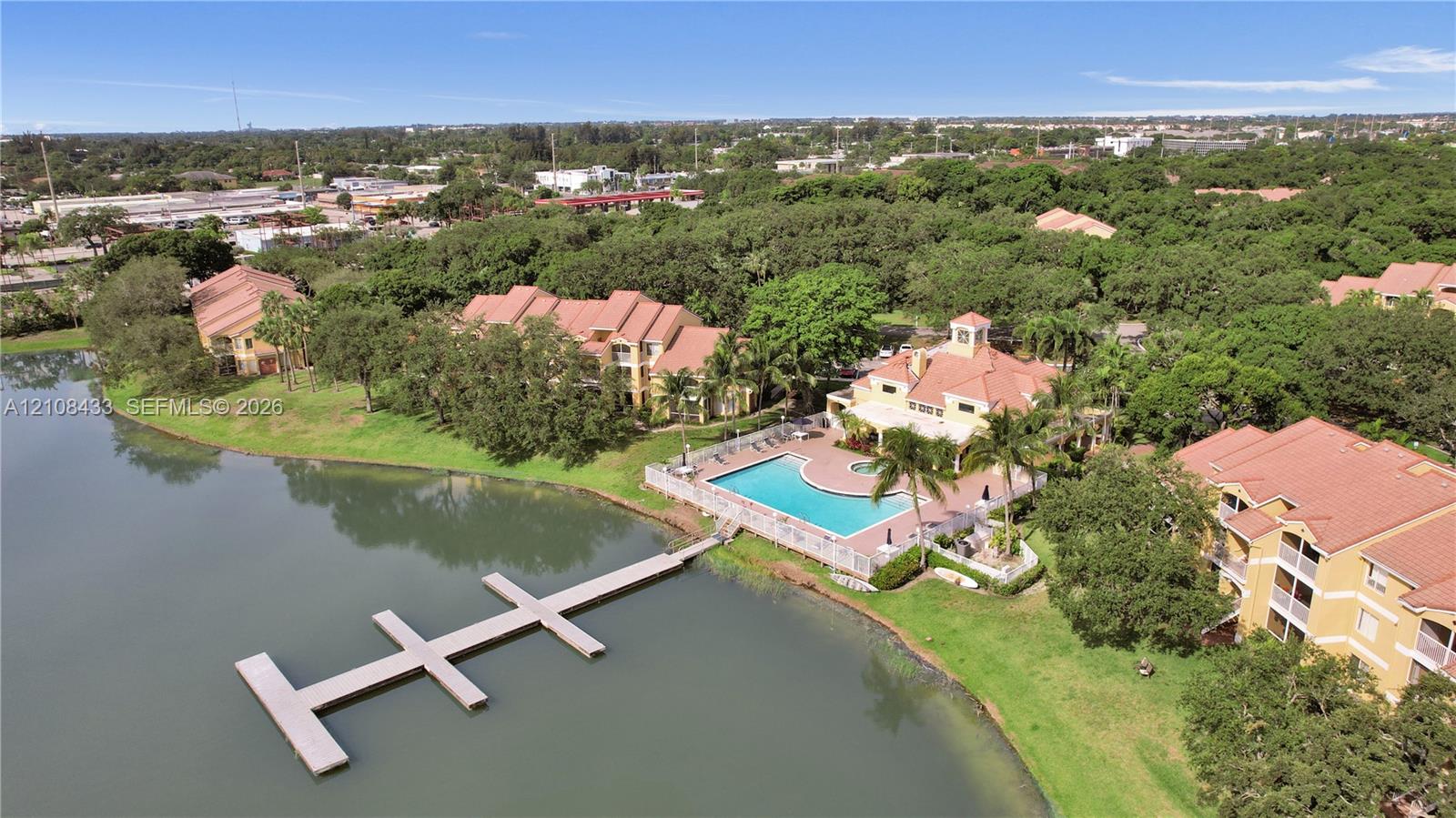 Aerial perspective featuring multi-story structures with tile roofing, an inground swimming pool, and a private dock extending into the lakefront Aerial perspective featuring multi-story structures with tile roofing, an inground swimming pool, and a private dock extending into the lakefront