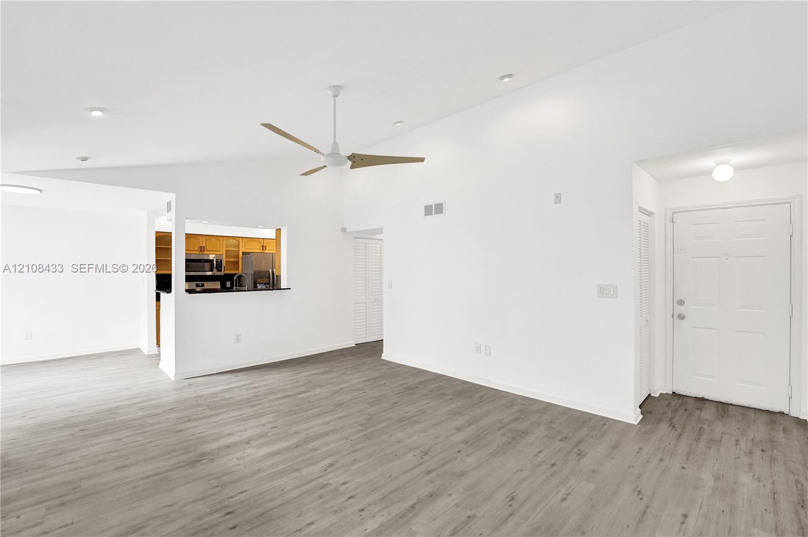 Vaulted ceilings, wood-finish flooring, ceiling fan with light fixture, recessed lighting, and pass-through counter opening to kitchen