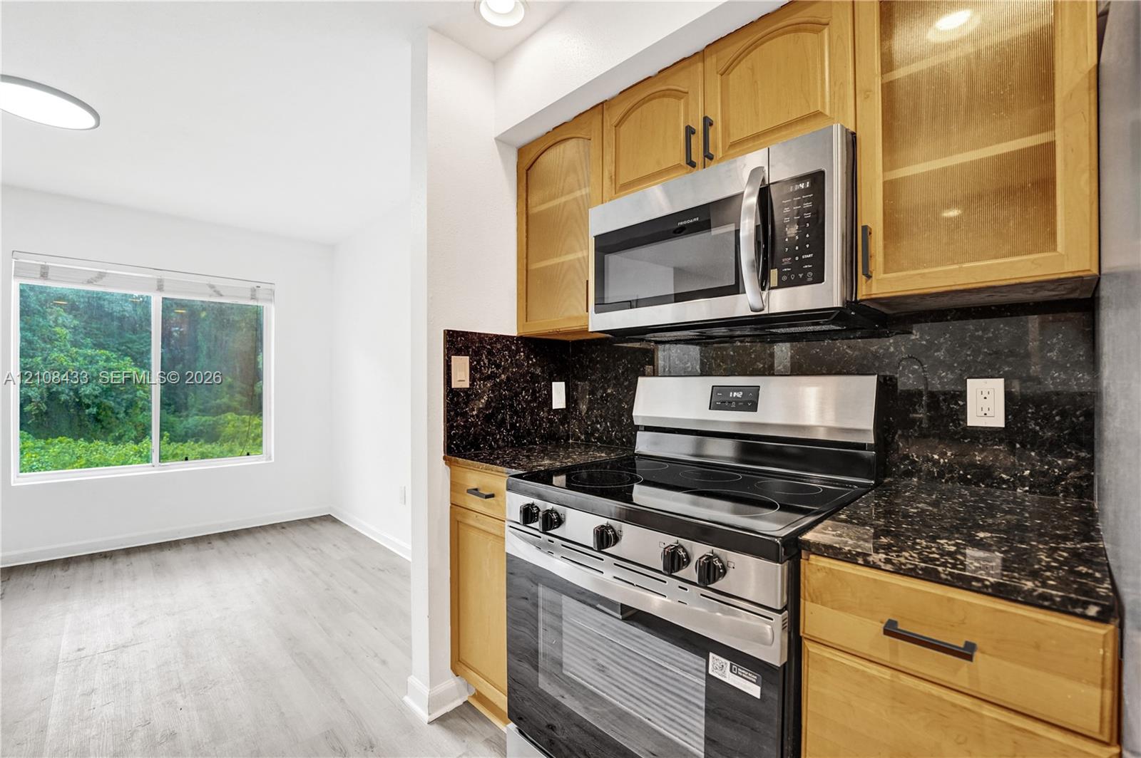 Kitchen featuring wood cabinetry, stainless steel appliances, dark stone countertops, and wood-finish flooring Kitchen featuring wood cabinetry, stainless steel appliances, dark stone countertops, and wood-finish flooring