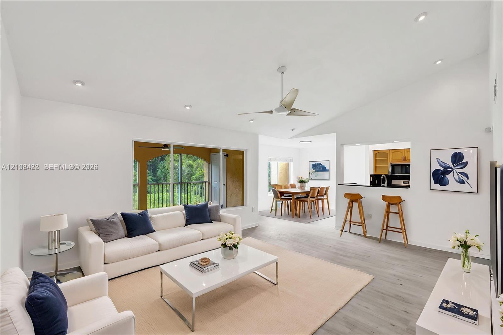 Living area featuring vaulted ceilings, recessed lighting, wood-finish flooring, a ceiling fan, and a pass-through opening to the kitchen Living area featuring vaulted ceilings, recessed lighting, wood-finish flooring, a ceiling fan, and a pass-through opening to the kitchen