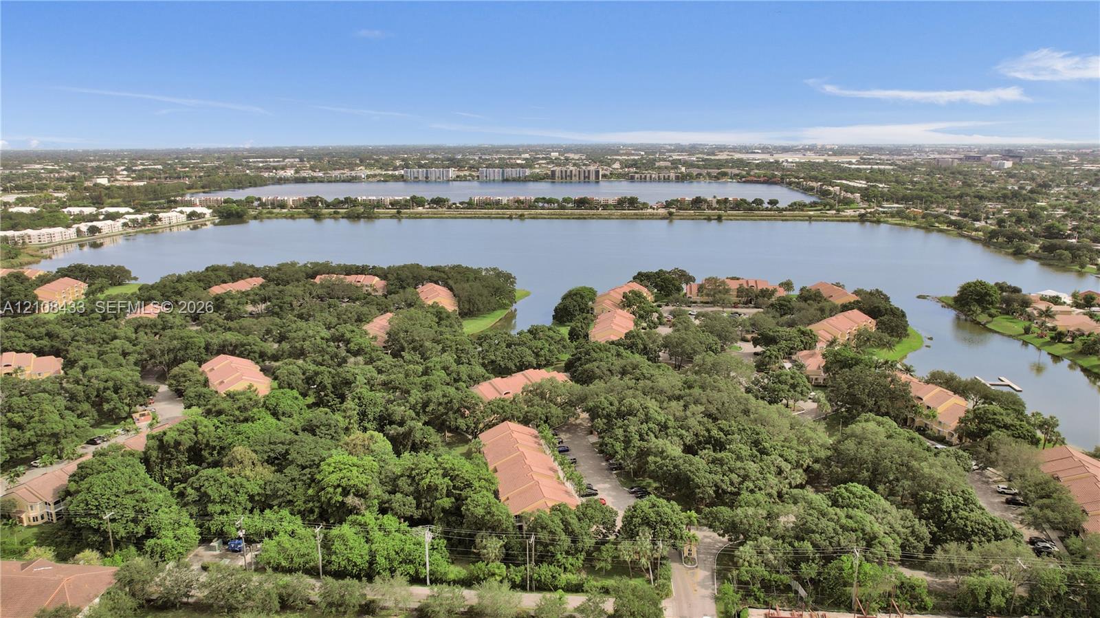 Aerial perspective of residential community featuring tile roofs, abundant mature tree canopy, paved streets, and expansive lake frontage