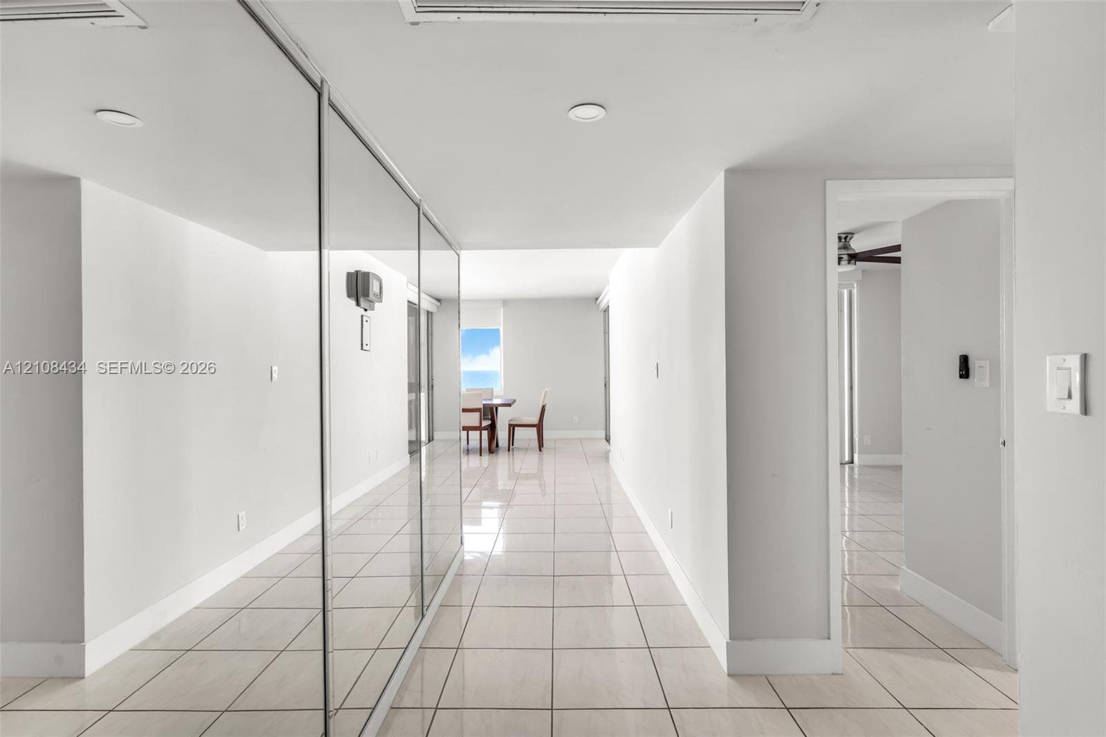 Interior hallway featuring light-toned tile flooring, floor-to-ceiling mirrored wall panels, and recessed lighting