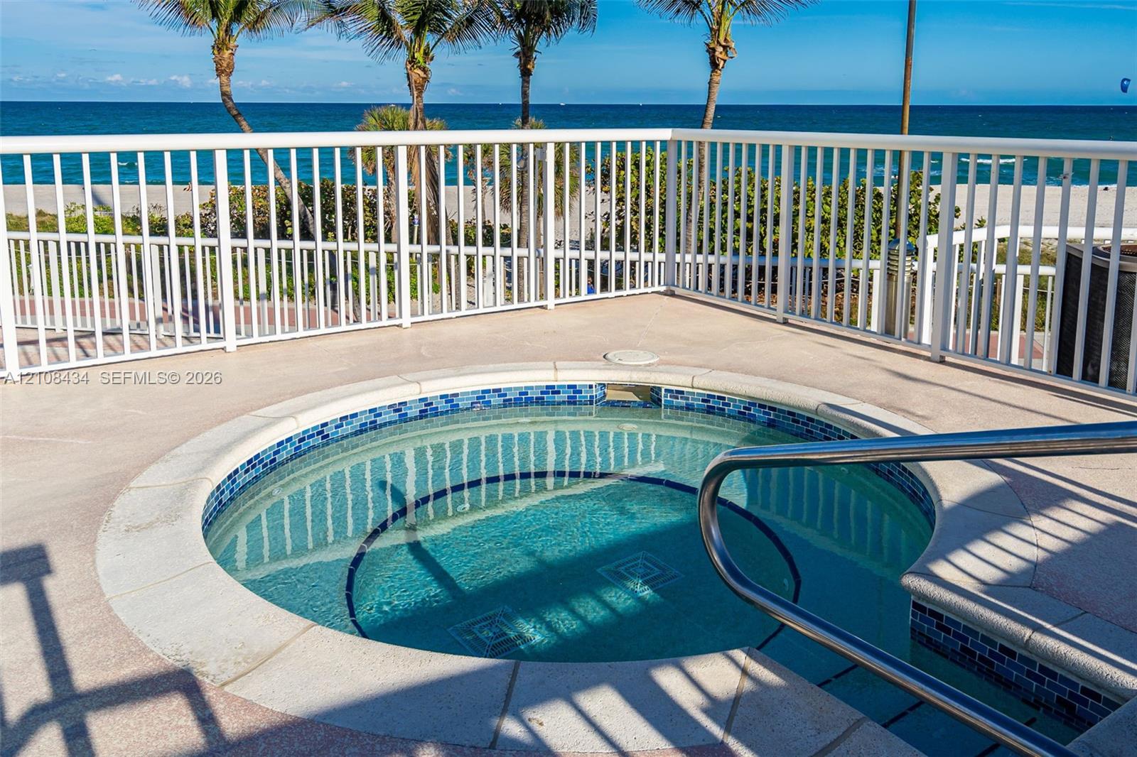 Circular jetted spa with blue tile surround, concrete decking, metal safety railing, and ocean backdrop
