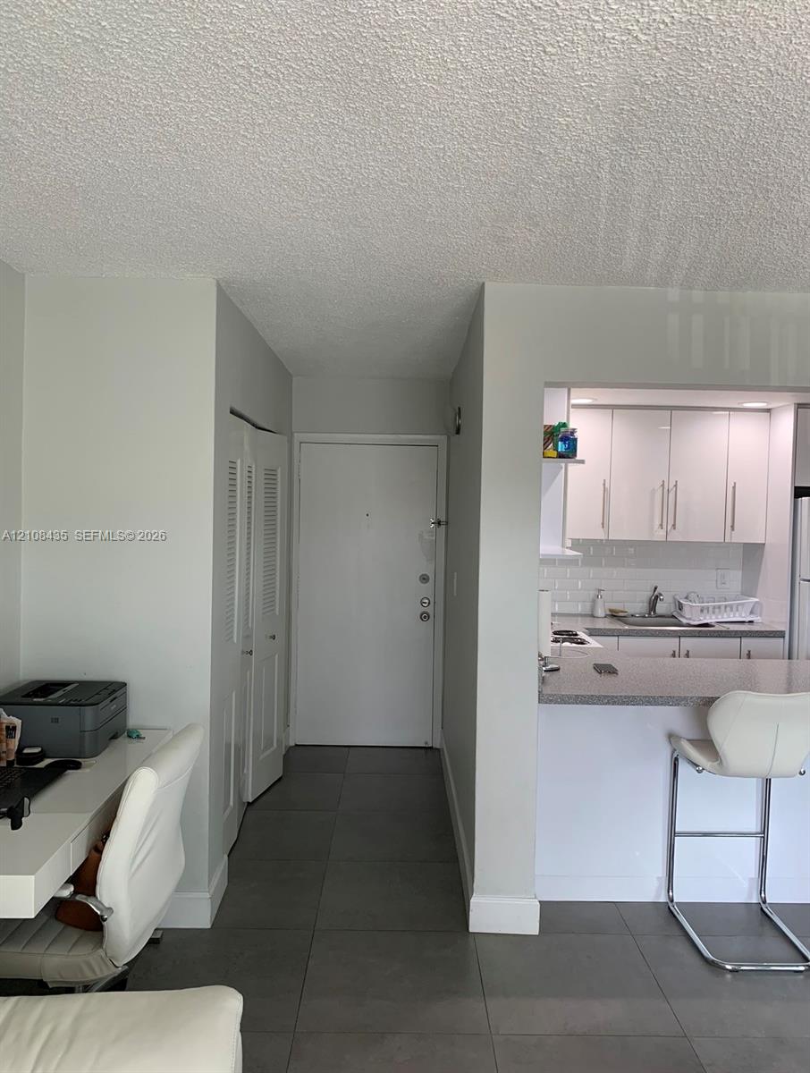 Entryway with large-format tile flooring, louvered-door closet, and kitchen featuring white cabinetry, subway tile backsplash, and stone-surface breakfast bar