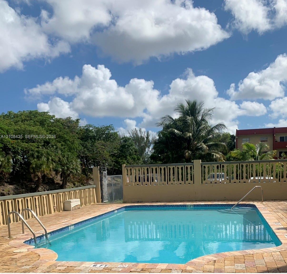 Inground swimming pool with tile trim, decorative concrete privacy wall, and brick paver decking