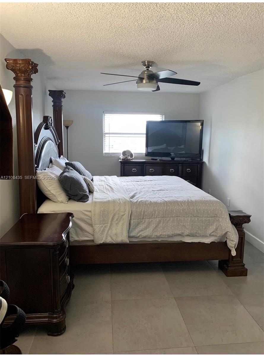 Neutral-toned tile flooring, multi-light ceiling fan with a brushed metal finish, and a window with horizontal blinds
