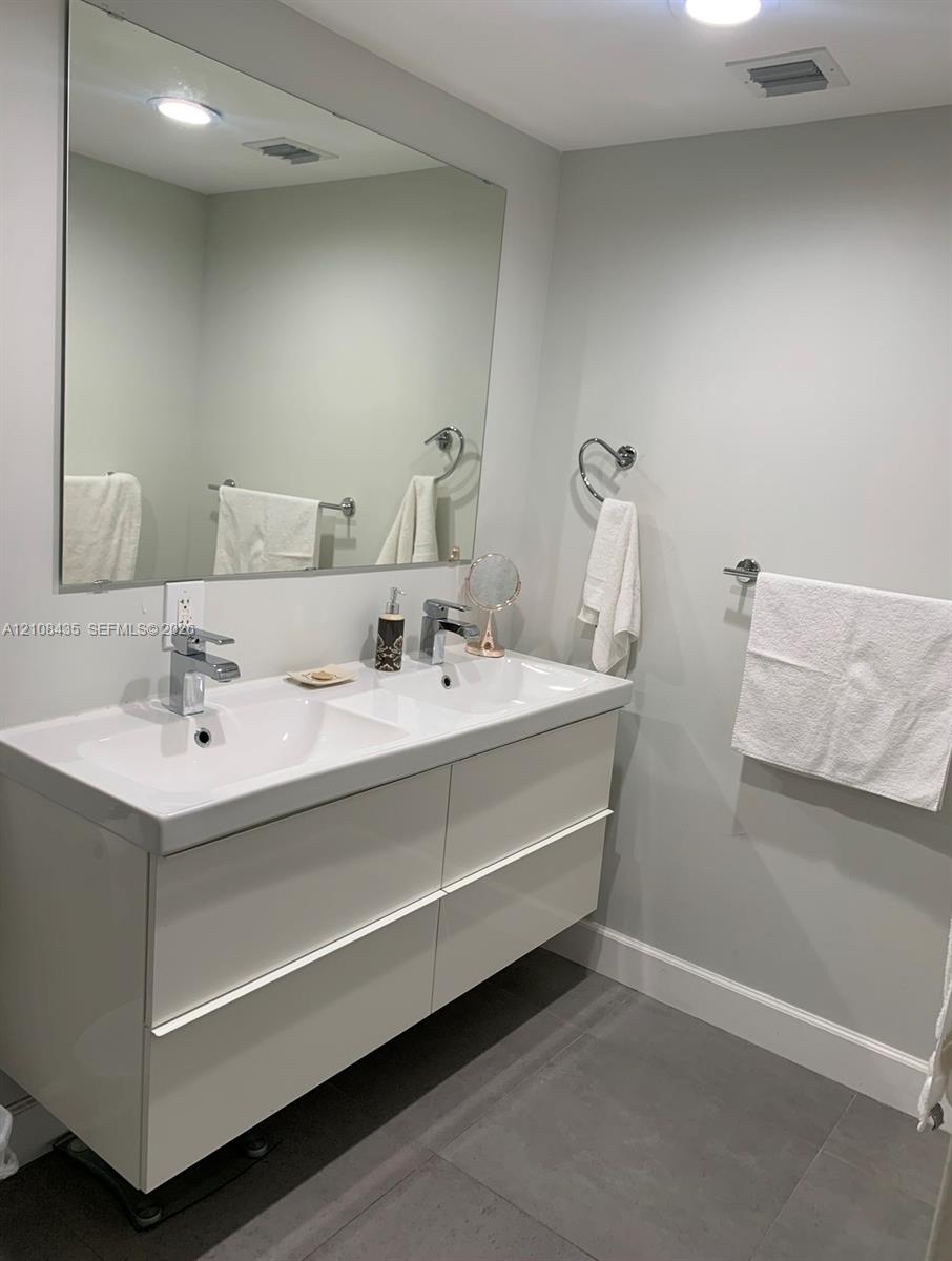 Floating double vanity with integrated dual sinks, polished chrome faucets, large wall-mounted mirror, and tile flooring