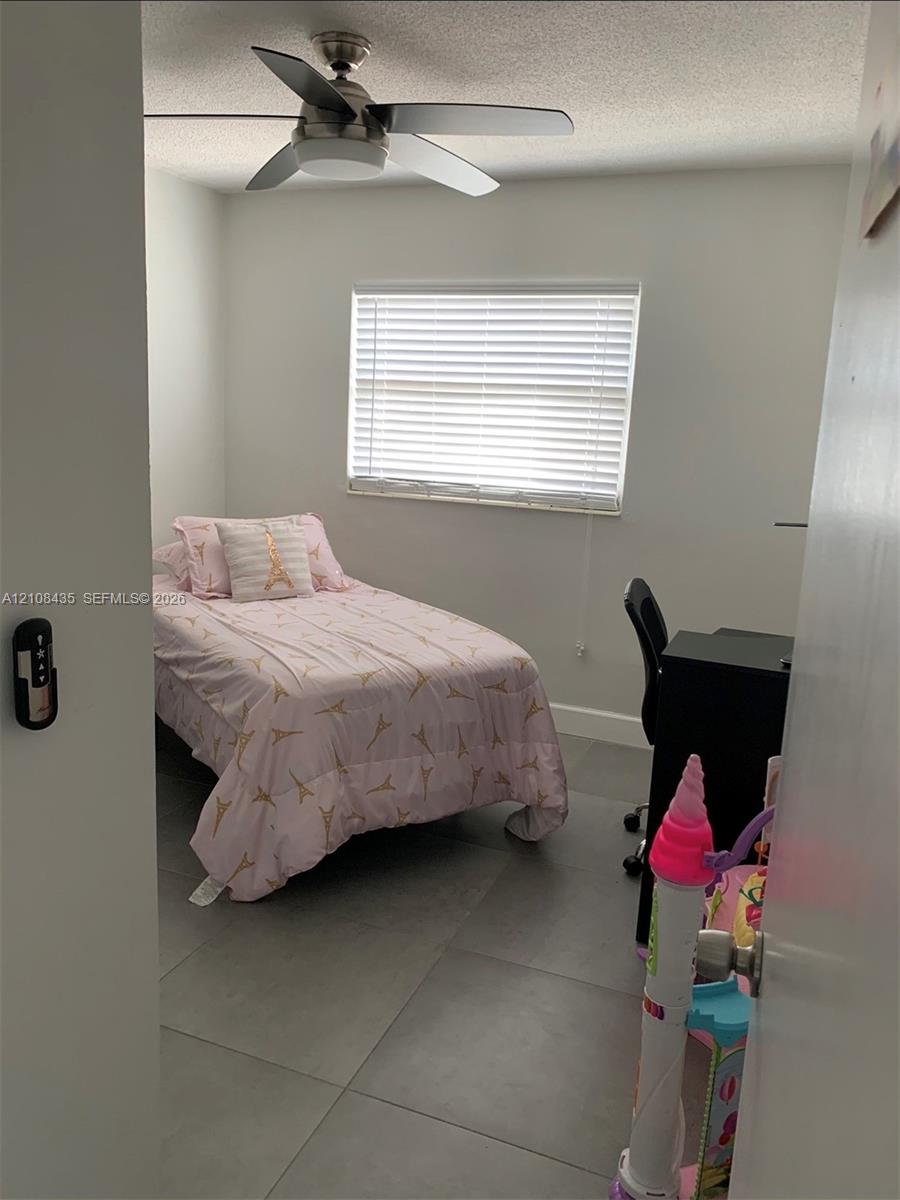 Neutral-toned room featuring large-format ceramic floor tiling, a multi-speed ceiling fan with integrated light fixture, and horizontal window blinds