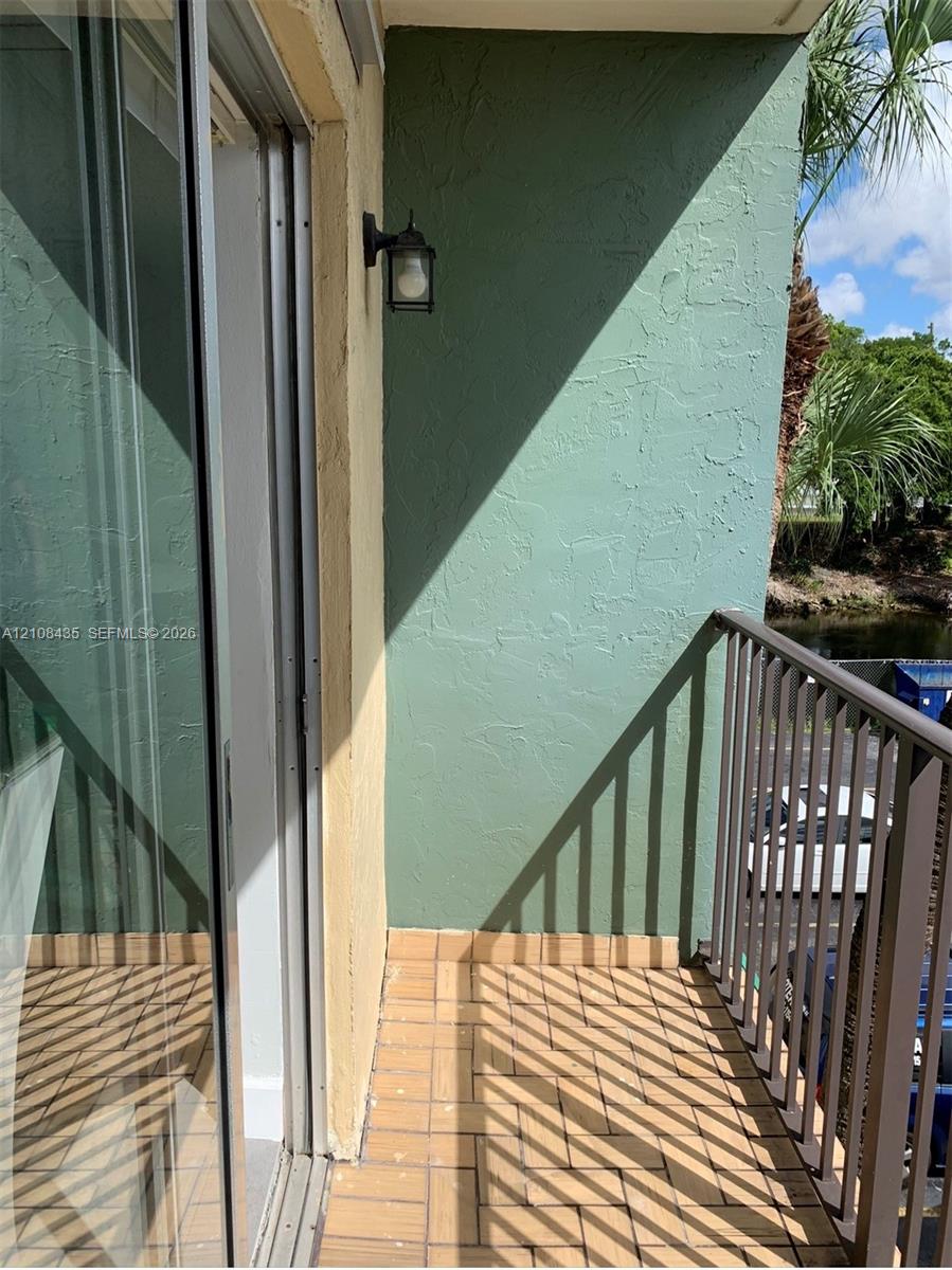 Private balcony featuring textured stucco walls, tiled flooring, metal railing, and a wall-mounted light fixture