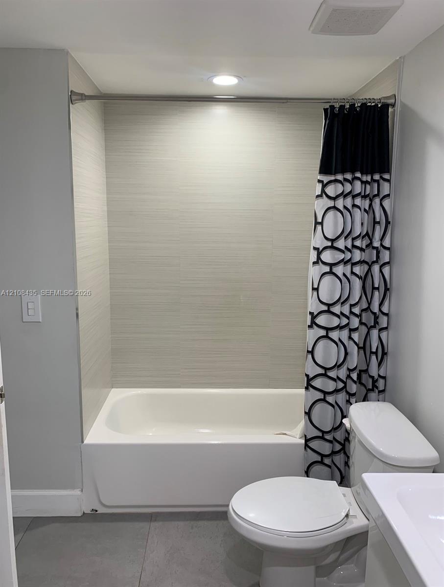 Bathtub surround featuring horizontally-aligned neutral-toned textured tile, recessed ceiling lighting, and large-format floor tile