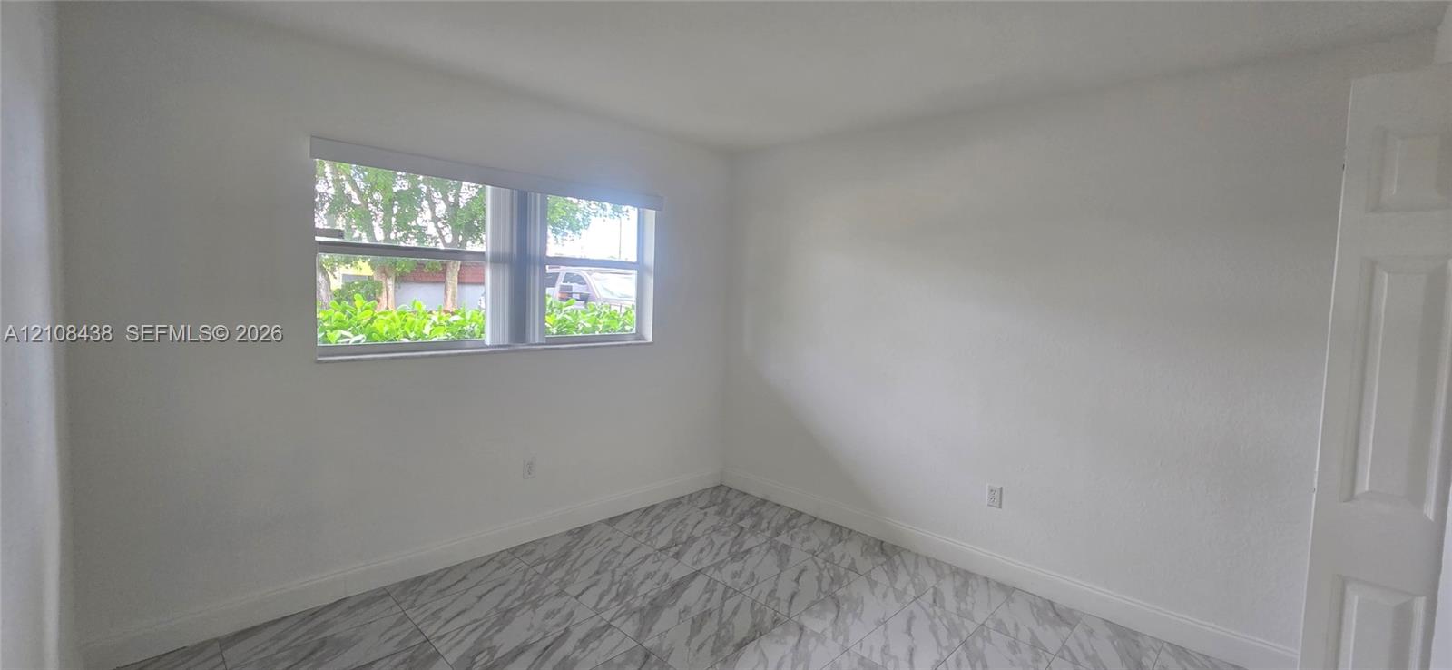 Interior space featuring light-colored tile flooring, smooth neutral wall finishes, and a single-pane horizontal window with integrated blinds
