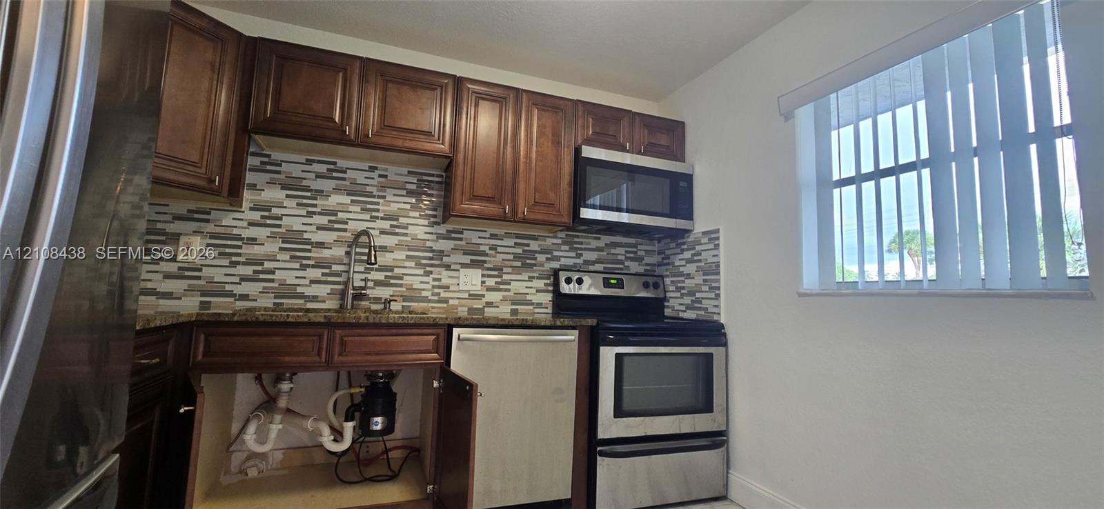 Kitchen featuring wood cabinetry, stone-finish countertops, decorative tile backsplash, and stainless steel appliances