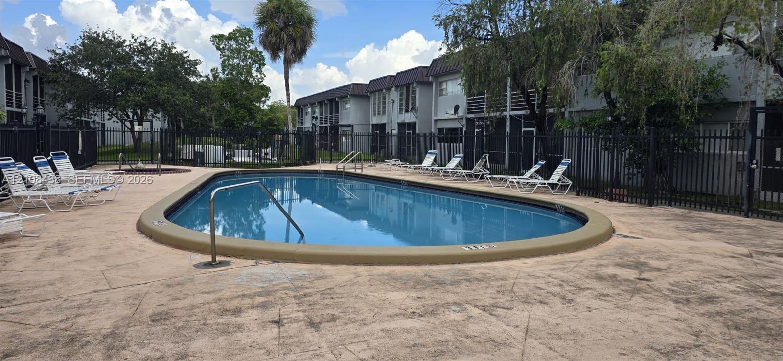 Oval swimming pool with metal handrails and paved pool deck, enclosed by perimeter fencing