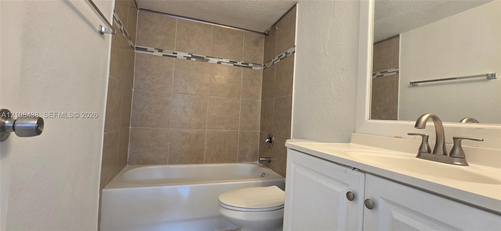 Bathroom featuring a white vanity cabinet with an integrated sink, satin-finish metal faucet, tub-shower combination with ceramic wall tiling, and decorative mosaic tile accent border