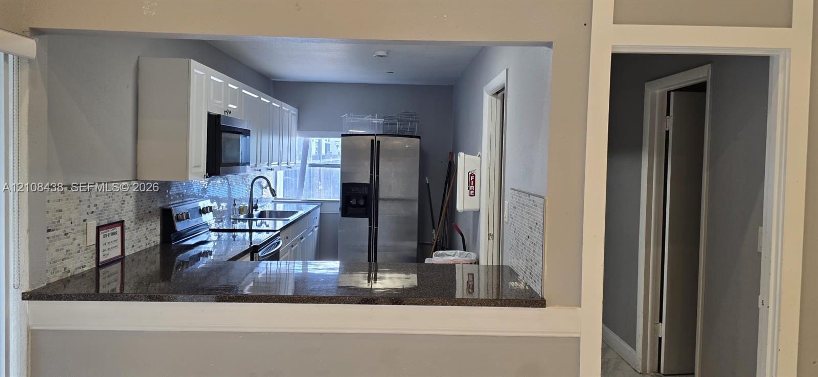 Kitchen featuring white cabinetry, dark stone-finish countertops, stainless steel appliances, and a tiled backsplash