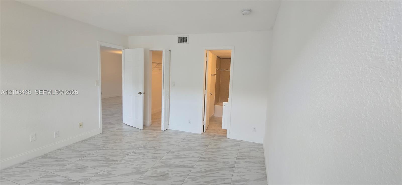 Interior space featuring large-format tile flooring with a neutral veined pattern, multiple closet entries, and a ceiling-mounted light fixture