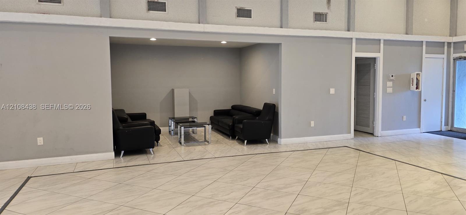 Large open interior space featuring recessed ceiling lighting, light-toned tile flooring with contrasting border inlay, and a dedicated recessed alcove