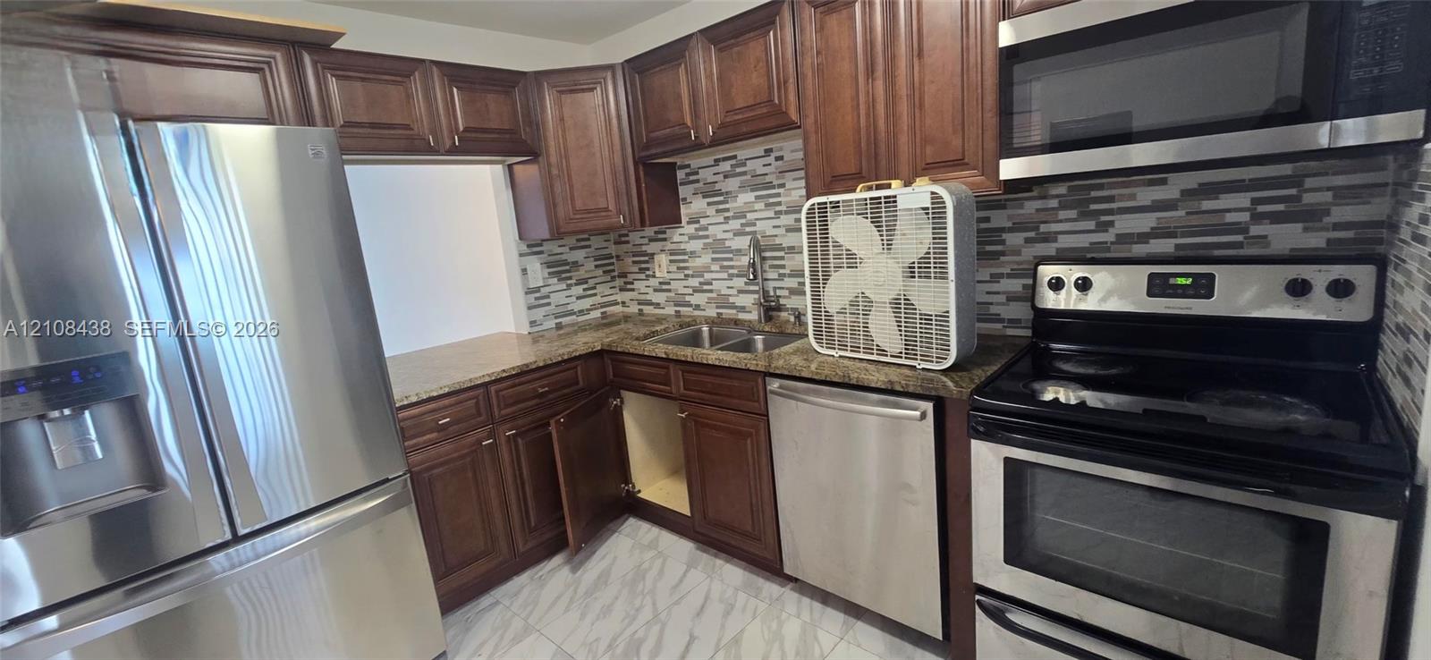 Kitchen featuring stained wood cabinetry, stone-finish countertops, stainless steel appliances, and a decorative tile backsplash