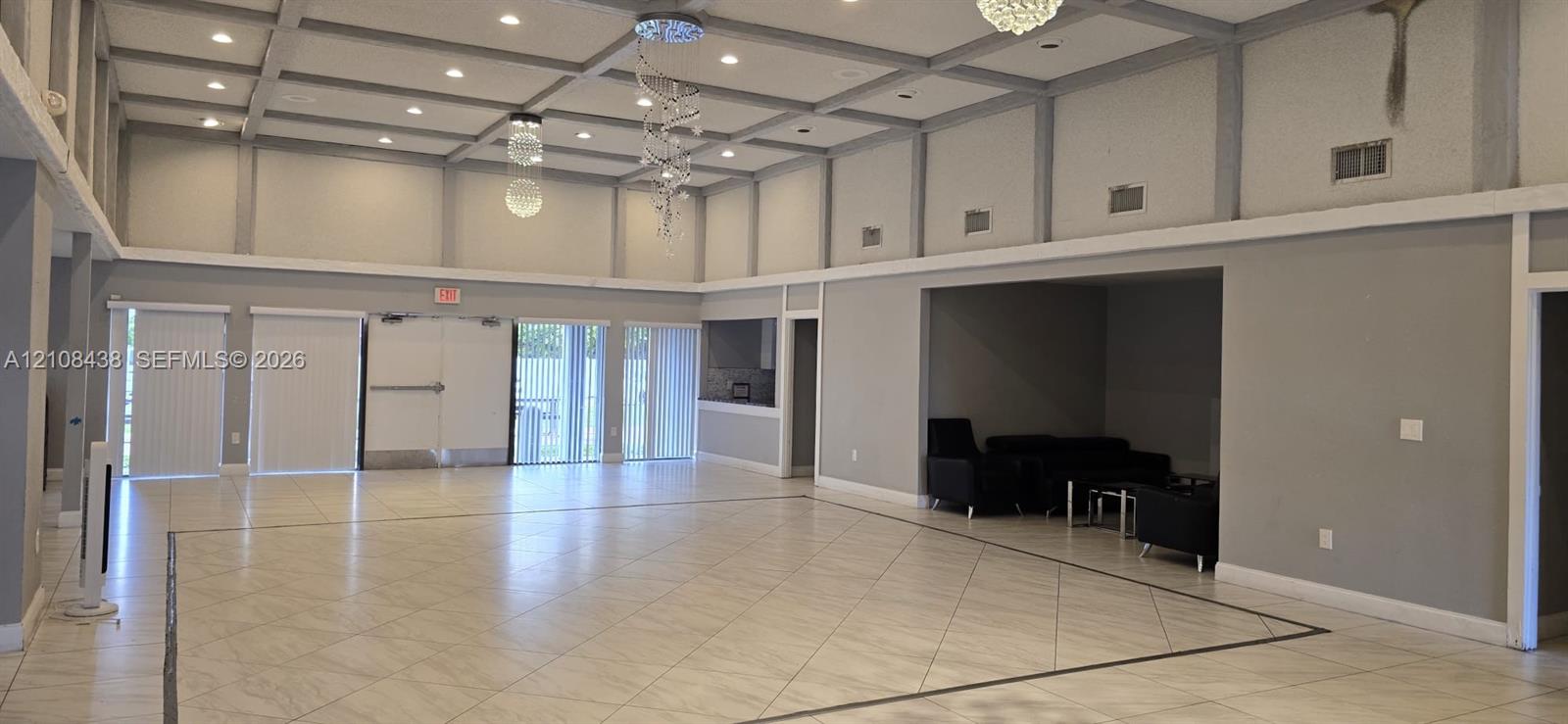 Large open-concept space featuring a coffered ceiling with recessed lighting, tile flooring, suspended decorative light fixtures, and glass sliding door access