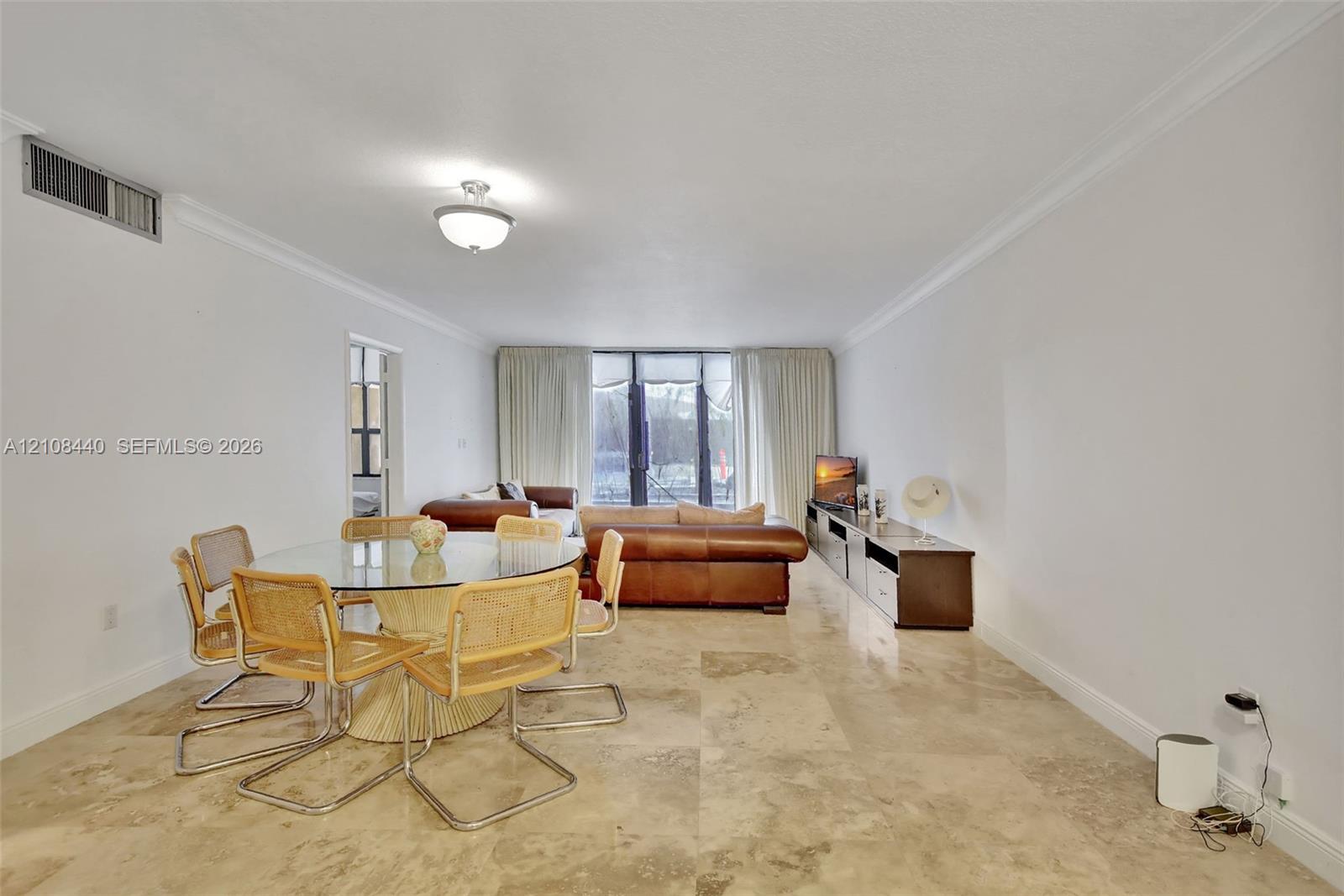 Open-concept interior featuring large-format stone flooring, crown molding, and floor-to-ceiling glass panel doors Open-concept interior featuring large-format stone flooring, crown molding, and floor-to-ceiling glass panel doors