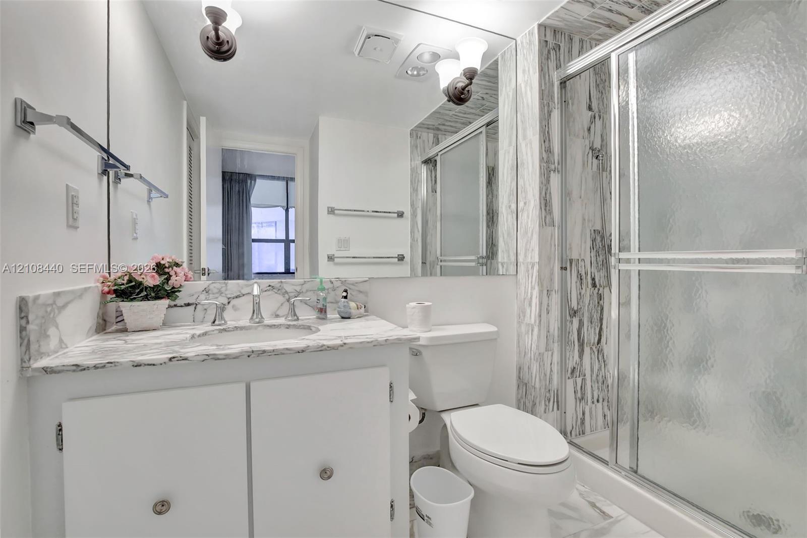 Bathroom featuring a stone-surface vanity with an integrated sink, floor-to-ceiling stone-tiled shower enclosure, chrome-finish sliding glass shower doors, wall-to-wall mirror, and wall-mounted light fixtures