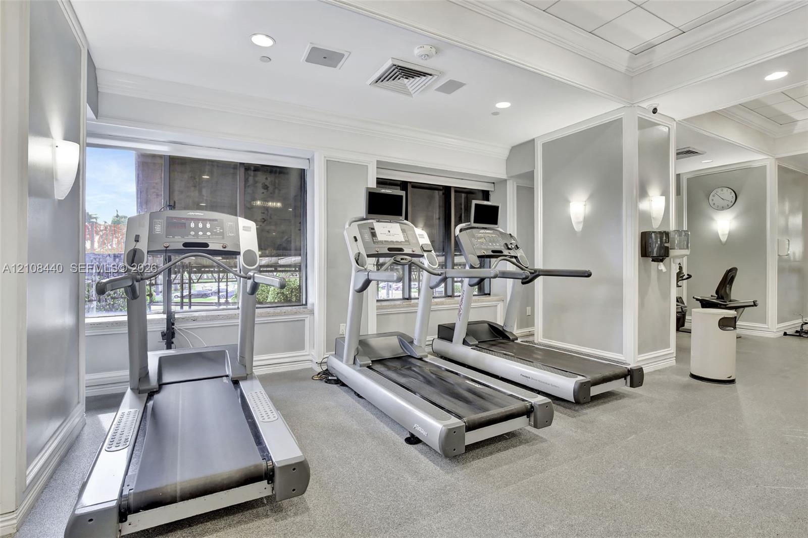 Fitness center featuring large windows, recessed ceiling lighting, wall-mounted sconces, and crown molding