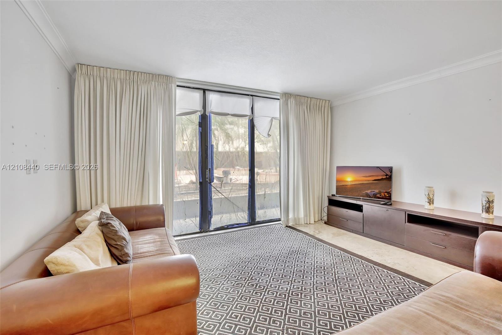 Living space featuring full-height floor-to-ceiling glass sliding doors, neutral stone-finish flooring, and crown molding Living space featuring full-height floor-to-ceiling glass sliding doors, neutral stone-finish flooring, and crown molding