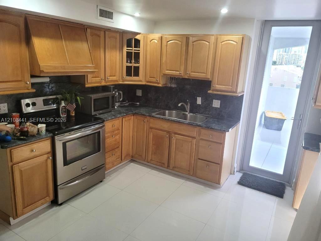 Kitchen featuring wood cabinetry, stone-finish countertops, stainless steel range, double-basin sink, and tile flooring
