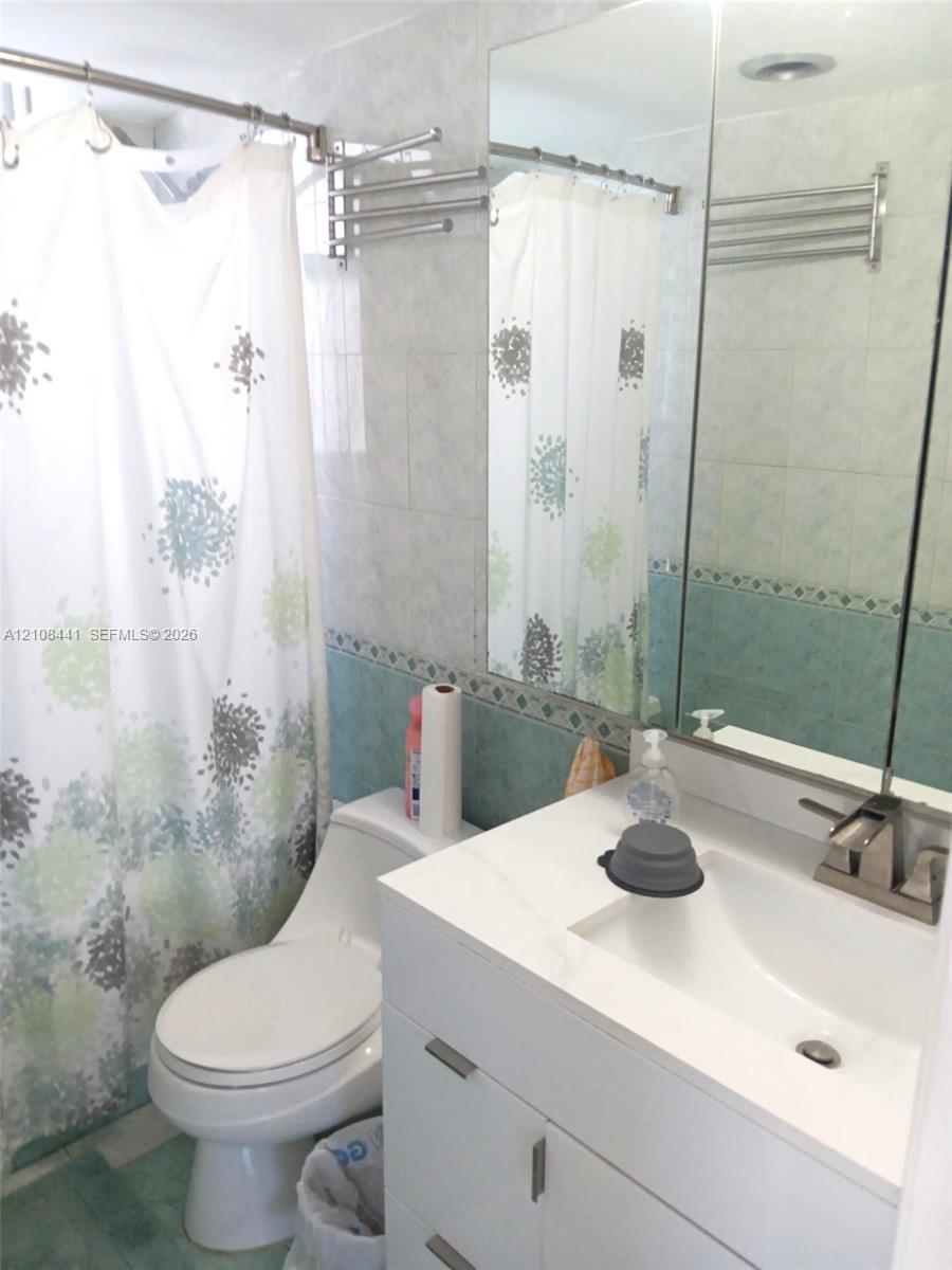 Bathroom featuring a white vanity cabinet with an integrated rectangular sink, a stone-finish countertop, a wall-mounted mirrored medicine cabinet, and tiled walls with decorative trim