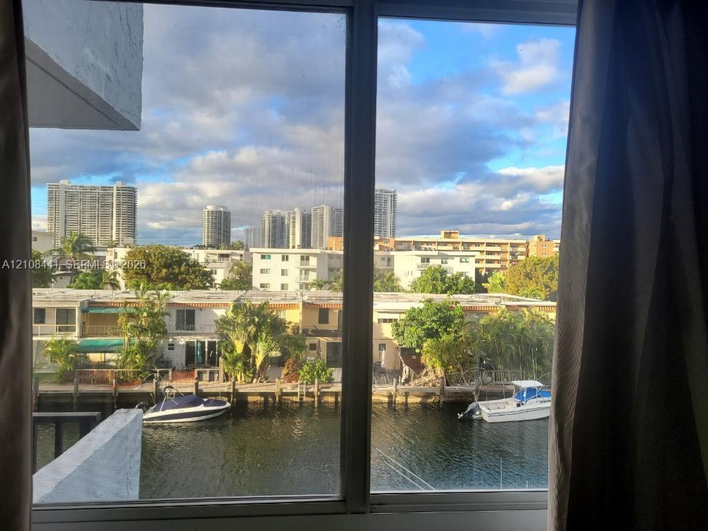 Large, multi-panel window framing a canal-side exterior featuring a private boat dock, deep-water waterway, and cityscape backdrop