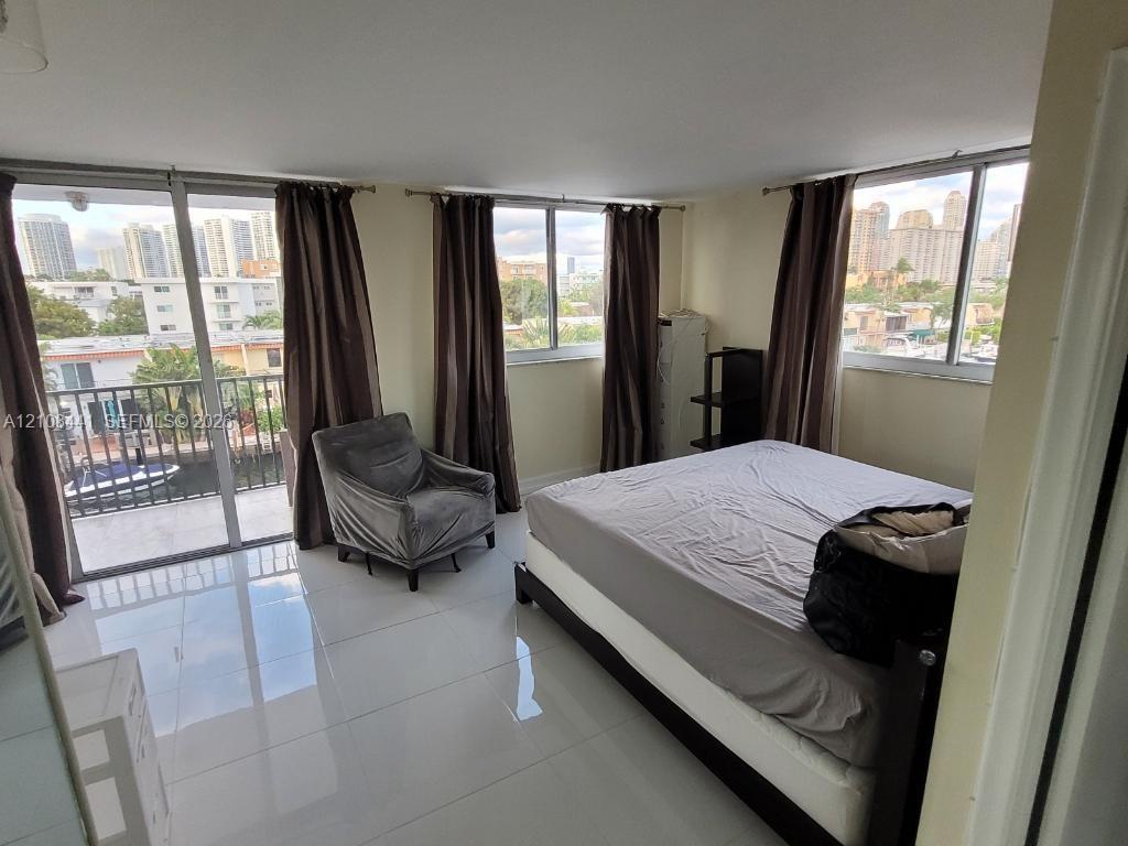 Spacious room featuring light-toned tile flooring, floor-to-ceiling windows, and access to a private balcony with a metal railing