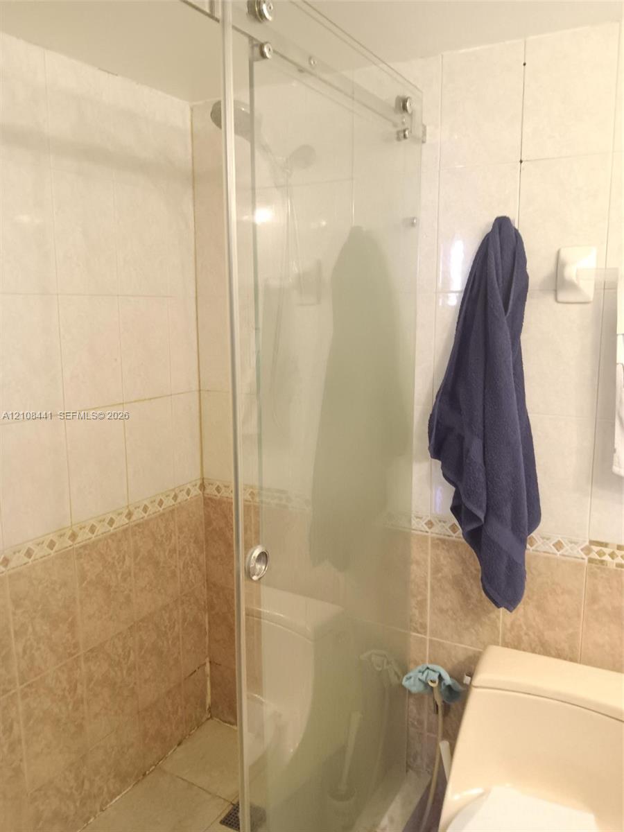 Walk-in shower featuring a frameless glass sliding door, wall-mounted shower head, and dual-tone ceramic tile surround