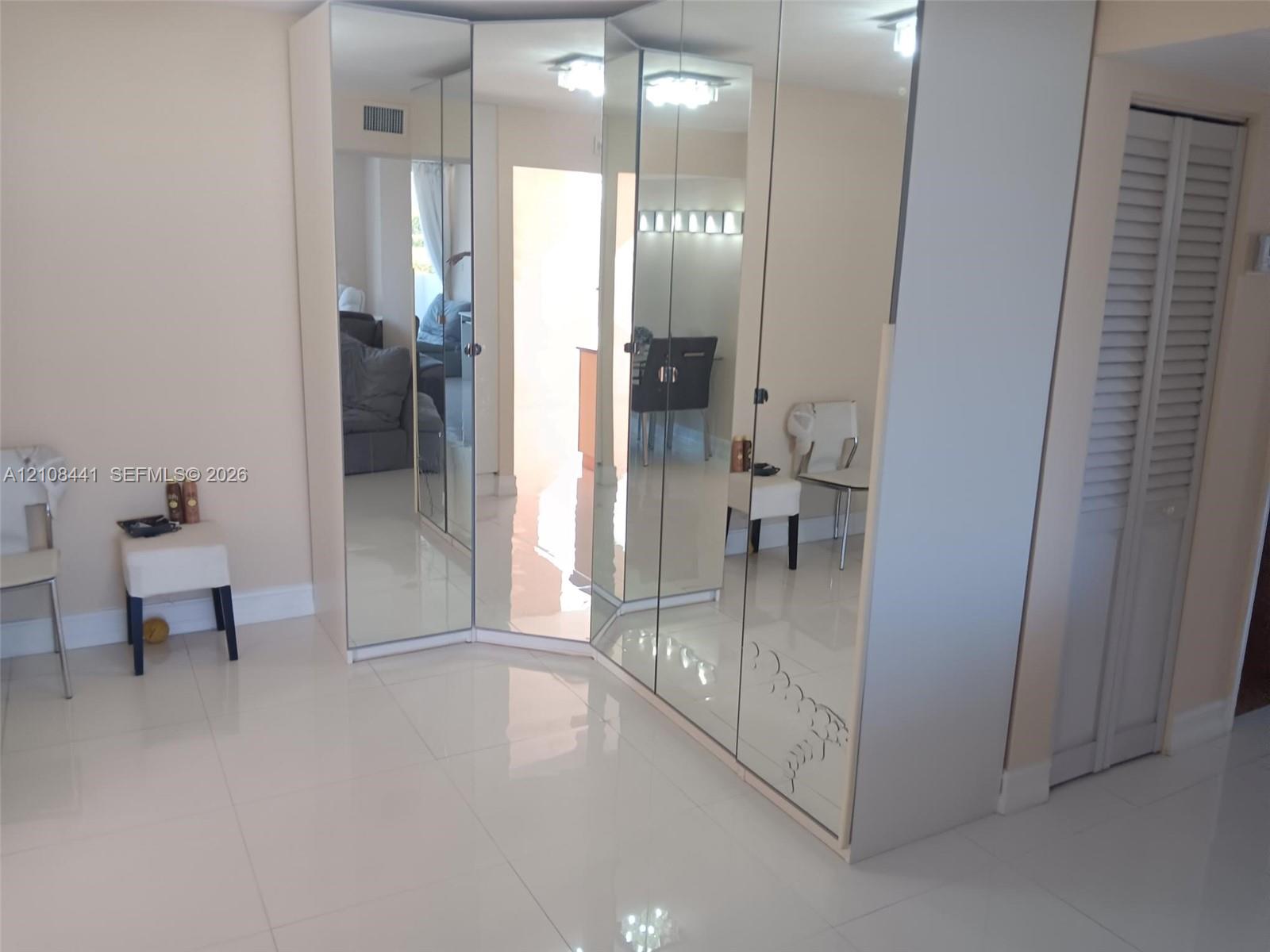 Floor-to-ceiling mirrored wardrobe featuring integrated cabinetry, reflective finish, and white tile flooring throughout, accented by louvered-panel closet doors and recessed lighting