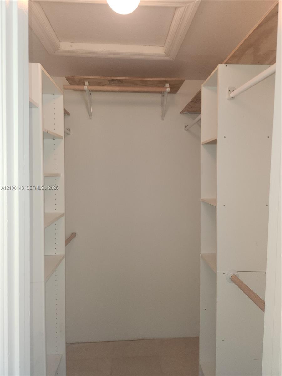 Storage space featuring white built-in shelving towers, wooden hanging rods, and upper wood-finish shelving