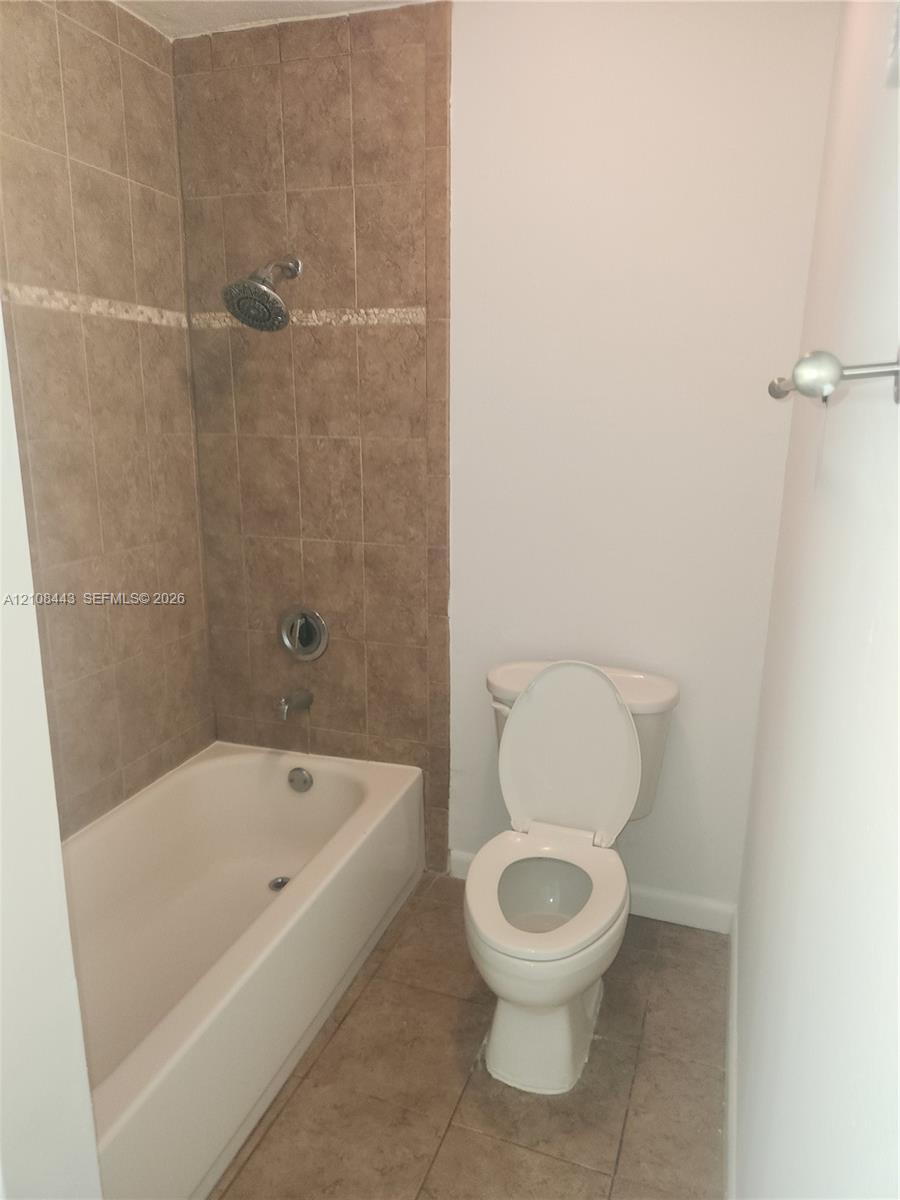 Bathtub with tile surround, decorative accent inlay, wall-mounted showerhead, and tile flooring