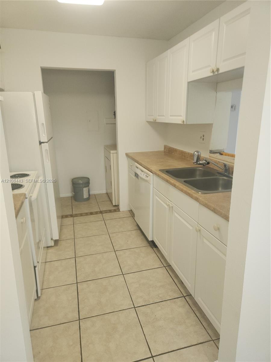 Kitchen featuring white cabinetry, solid-surface countertops, dual-basin stainless steel sink, built-in dishwasher, and ceramic tile flooring