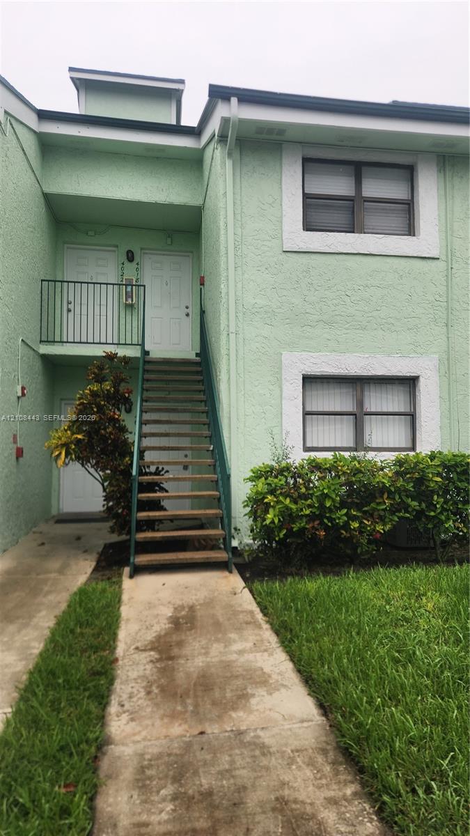 Two-story exterior featuring a textured stucco finish, white window trim, a metal staircase with railings, and a concrete walkway