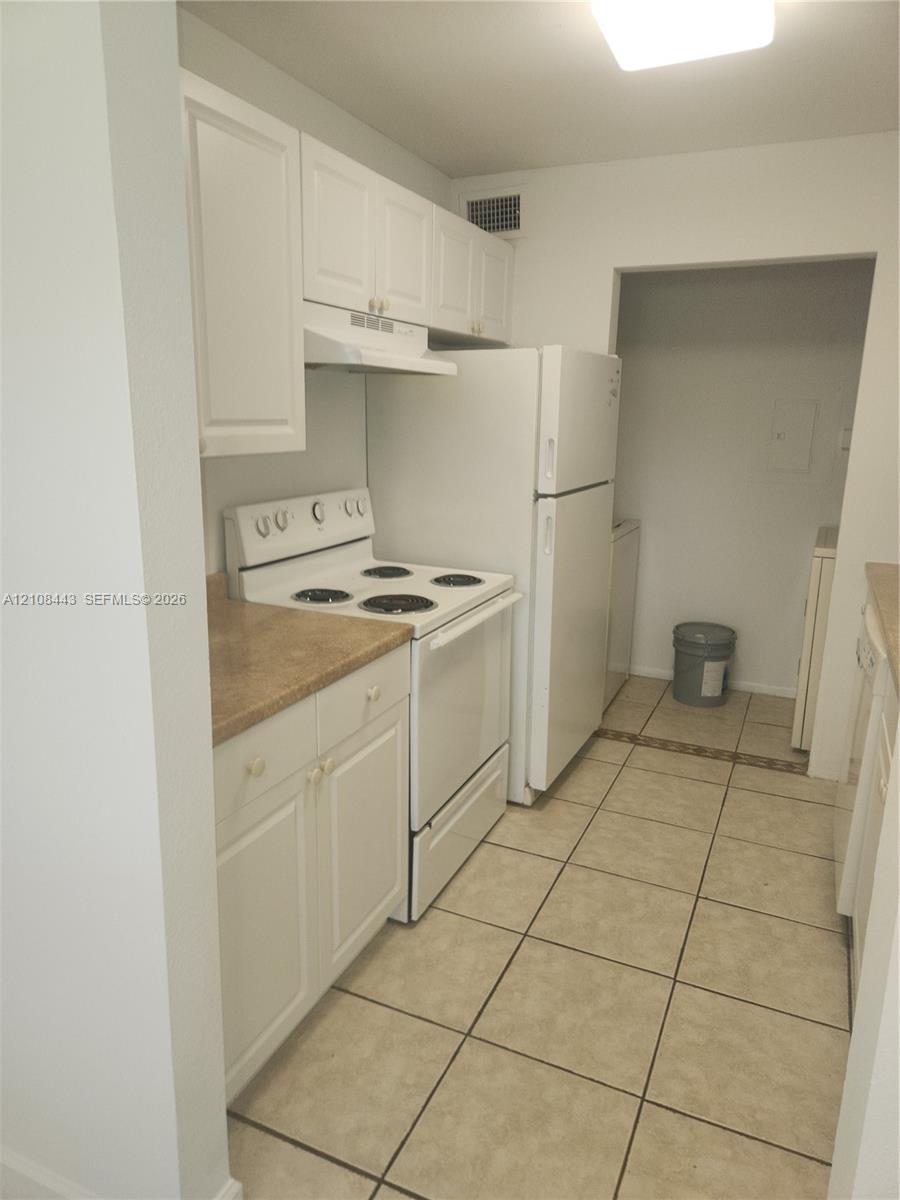 Kitchen featuring white cabinetry, solid-surface countertops, tile flooring, and integrated white appliances Kitchen featuring white cabinetry, solid-surface countertops, tile flooring, and integrated white appliances