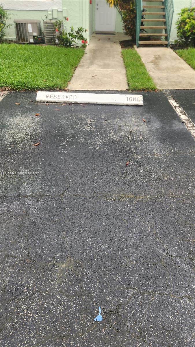 Designated parking space with concrete bumper, asphalt surface, and concrete walkway
