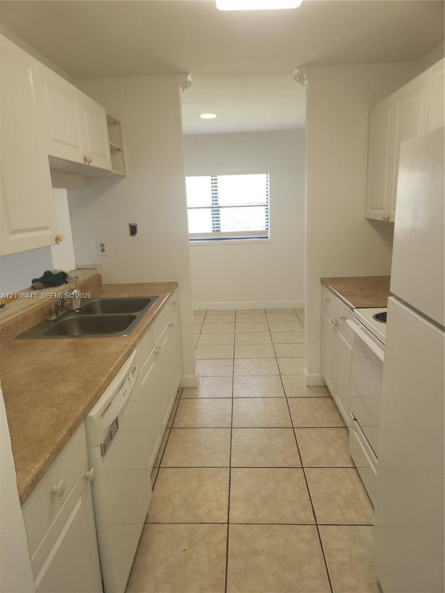 Kitchen featuring white cabinetry, solid-surface countertops, dual-basin stainless steel sink, and ceramic tile flooring Kitchen featuring white cabinetry, solid-surface countertops, dual-basin stainless steel sink, and ceramic tile flooring