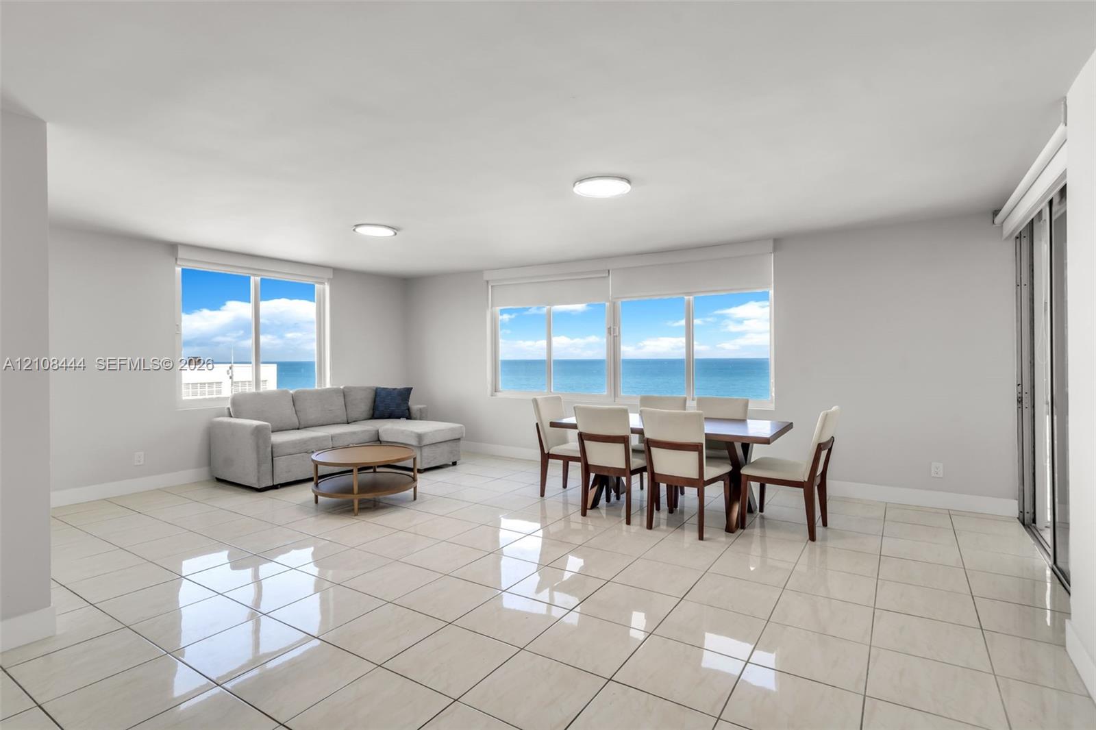 Open-concept living space featuring high-gloss tile flooring, floor-to-ceiling windows, and panoramic ocean water scenery