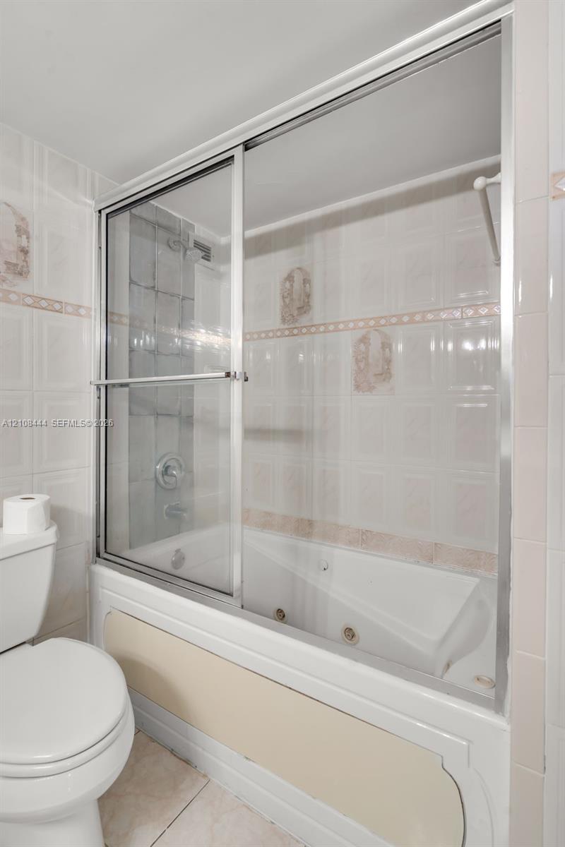 Jetted soaking tub with integrated shower, sliding glass enclosure, and wall-mounted plumbing fixtures surrounded by ceramic tile wall accents