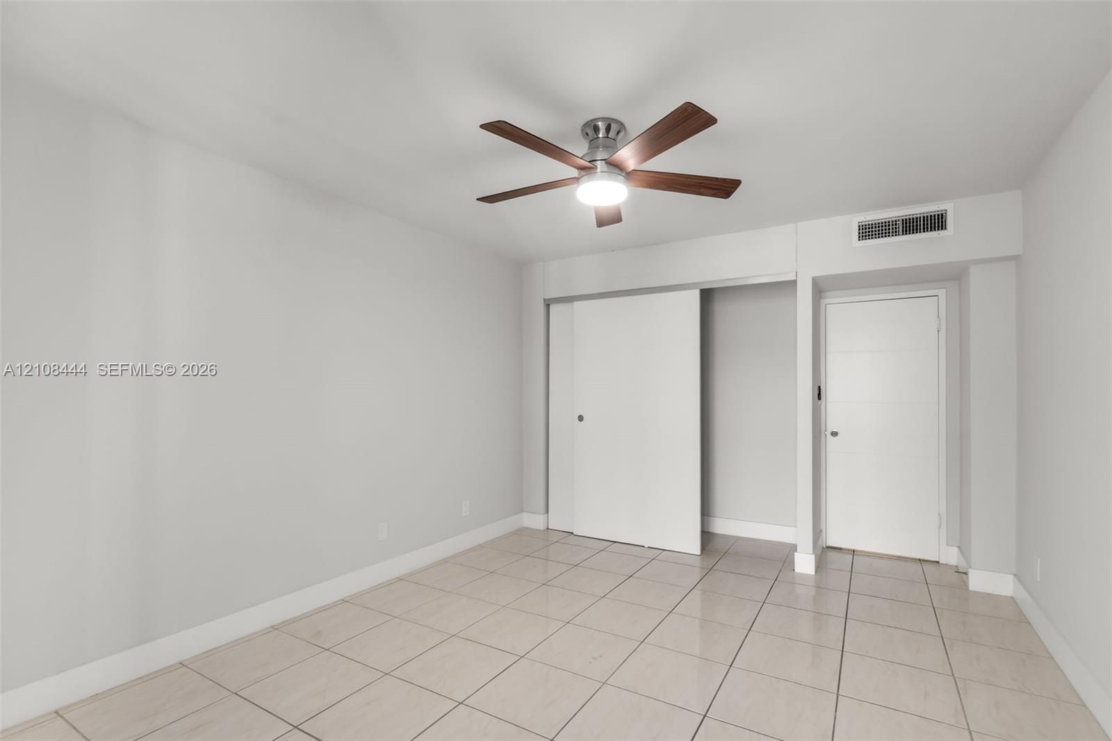 Neutral-toned room featuring large-format tile flooring, a multi-blade ceiling fan with integrated lighting, a sliding-door closet, and a contemporary flat-panel door