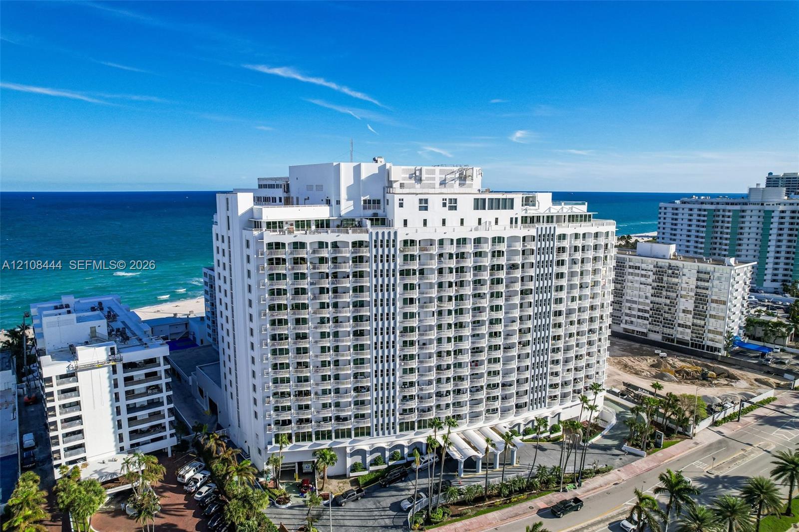 High-rise building featuring white masonry exterior, multiple levels of private balconies, arched ground-floor portico, and direct coastal proximity
