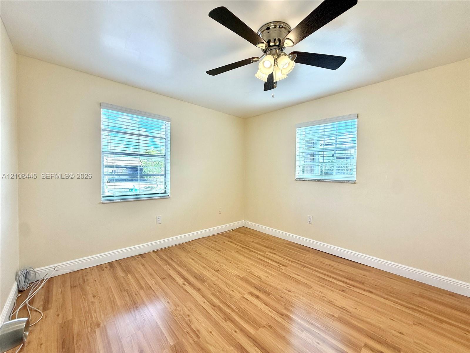 Bedroom 2 featuring wood-finish flooring, two windows with horizontal blinds, and a central ceiling fan with multi-light fixture